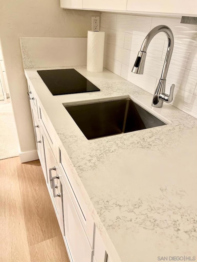 kitchen with black electric cooktop, white cabinetry, sink, and light stone counters