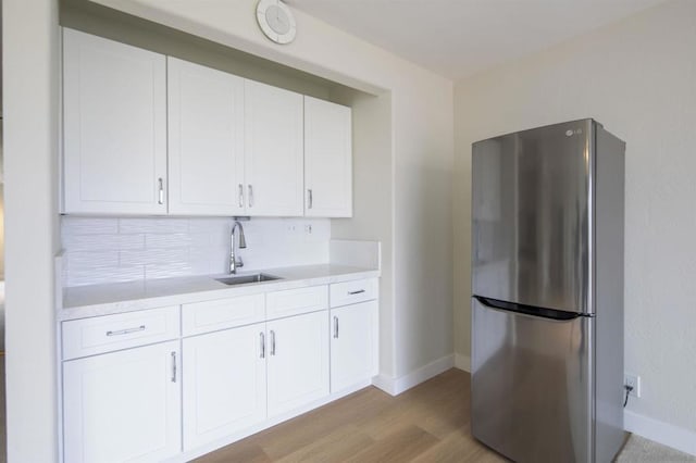 kitchen with sink, stainless steel fridge, light hardwood / wood-style flooring, white cabinetry, and decorative backsplash