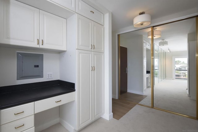 kitchen with white cabinetry, light colored carpet, built in desk, and electric panel