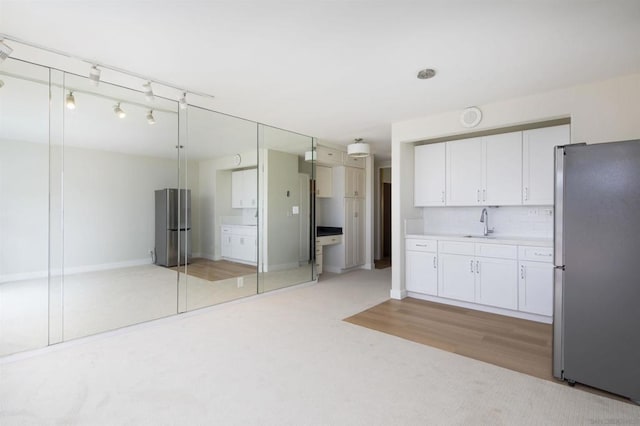 kitchen with stainless steel refrigerator, white cabinetry, sink, and backsplash