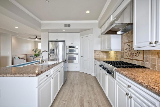 kitchen featuring wall chimney exhaust hood, a kitchen island with sink, white cabinets, appliances with stainless steel finishes, and sink