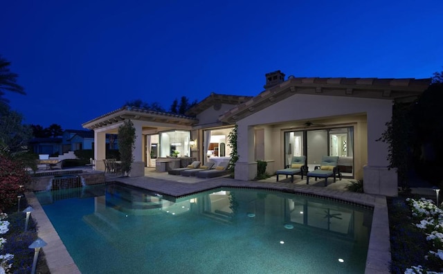 pool at night with ceiling fan, a patio, and an in ground hot tub