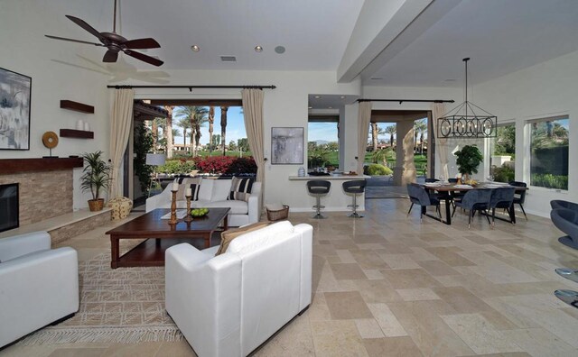 living room featuring ceiling fan with notable chandelier and a stone fireplace