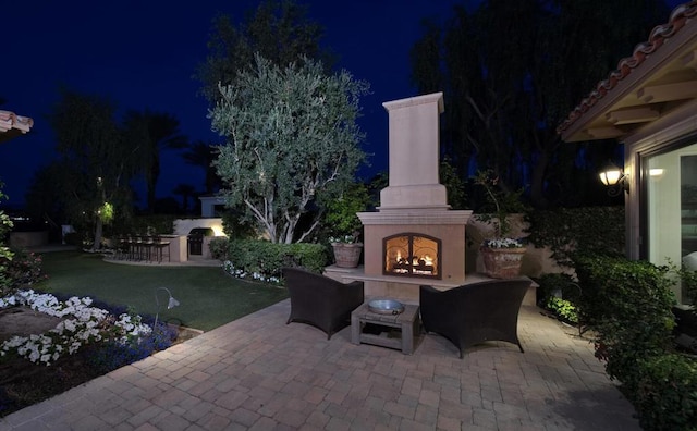 patio at night with exterior fireplace and area for grilling