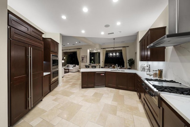 kitchen featuring kitchen peninsula, stainless steel appliances, decorative light fixtures, wall chimney exhaust hood, and sink