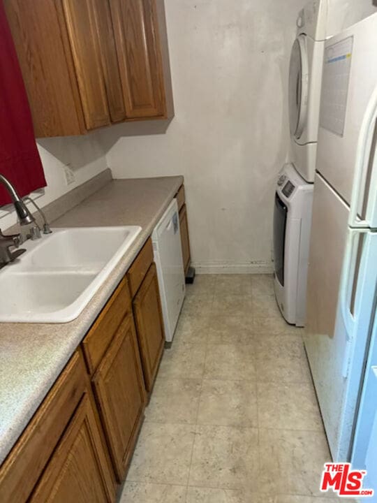 kitchen with stacked washer / dryer, sink, and white appliances