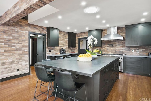 kitchen with brick wall, high end stainless steel range oven, a center island, wall chimney range hood, and light wood-type flooring