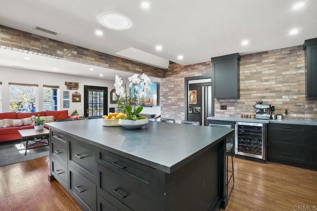 kitchen with wine cooler, brick wall, wood-type flooring, and a center island