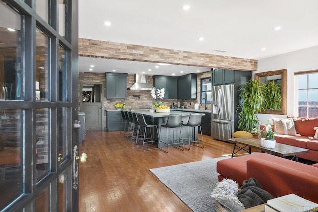 kitchen with wall chimney exhaust hood, sink, stainless steel fridge, a kitchen breakfast bar, and hardwood / wood-style floors