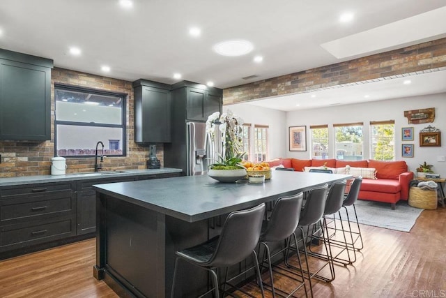 kitchen with light wood finished floors, a kitchen island, a kitchen breakfast bar, open floor plan, and a sink