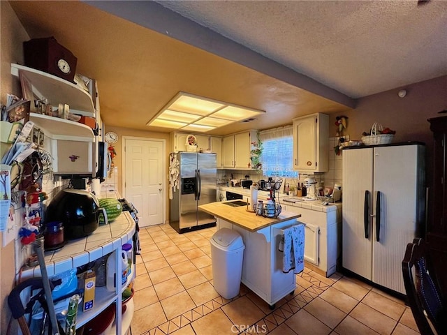 kitchen with white fridge, light tile patterned floors, tile countertops, stainless steel fridge, and white cabinets