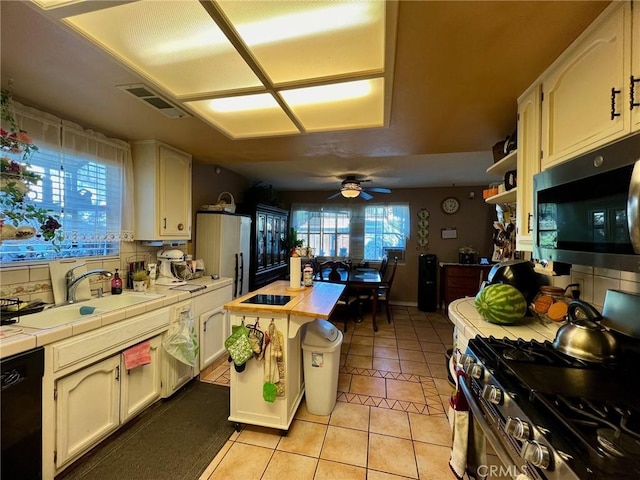 kitchen featuring appliances with stainless steel finishes, sink, tile countertops, ceiling fan, and light tile patterned floors