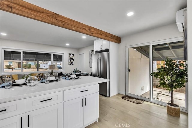 kitchen with a wall unit AC, light hardwood / wood-style floors, beamed ceiling, high end fridge, and white cabinets