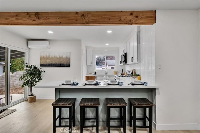 kitchen featuring an AC wall unit, a kitchen breakfast bar, white cabinets, and kitchen peninsula