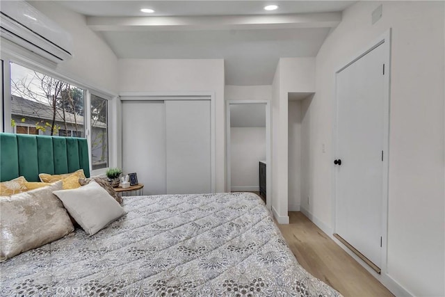 bedroom featuring light wood-type flooring, a closet, a wall mounted AC, and lofted ceiling with beams