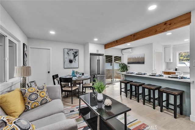 living room with beamed ceiling, a wall mounted AC, and light wood-type flooring