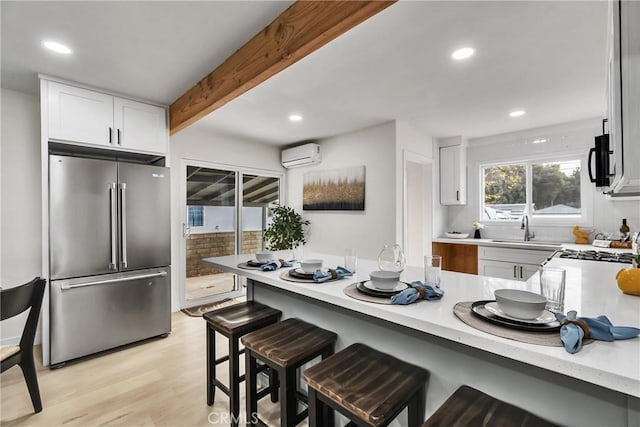 kitchen with kitchen peninsula, high end fridge, a wall unit AC, a kitchen breakfast bar, and beam ceiling