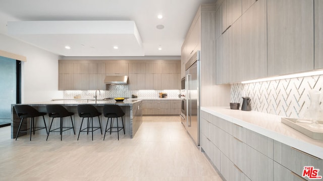 kitchen with backsplash, extractor fan, sink, a kitchen breakfast bar, and light brown cabinets