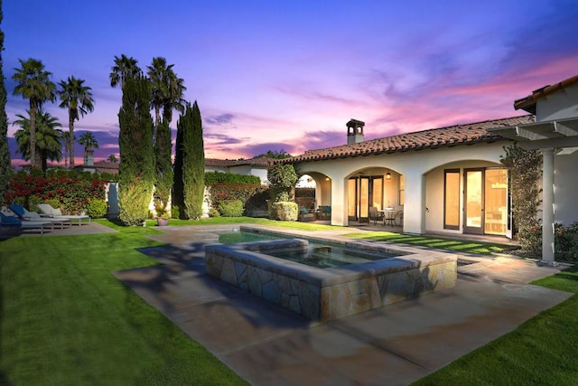 back house at dusk featuring a patio area, a swimming pool with hot tub, and a yard