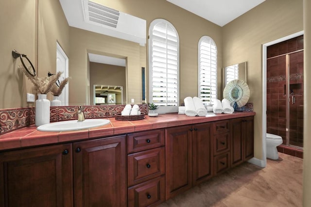 bathroom featuring a shower with door, toilet, vanity, and tasteful backsplash