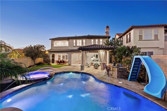 back house at dusk featuring pool water feature, a patio area, a pool with hot tub, and an outdoor bar