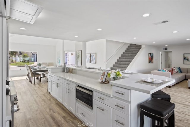 kitchen featuring white cabinetry, light wood-type flooring, a breakfast bar, stainless steel microwave, and a center island with sink