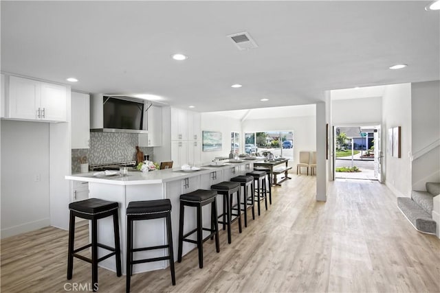 kitchen with a kitchen bar, white cabinetry, decorative backsplash, and wall chimney exhaust hood