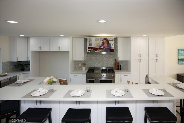 kitchen with exhaust hood, white cabinetry, a breakfast bar area, tasteful backsplash, and range with two ovens