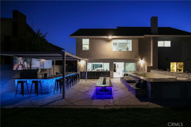 back house at night featuring a patio and exterior bar