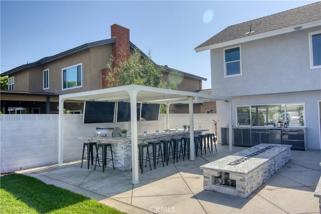 back of property with an outdoor fire pit, a bar, area for grilling, and a patio