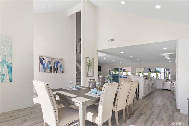 dining space with high vaulted ceiling and light hardwood / wood-style flooring