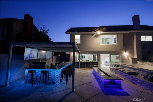 back house at dusk with a patio area and exterior bar