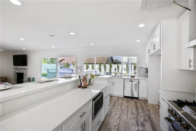 kitchen with white cabinetry, light wood-type flooring, appliances with stainless steel finishes, plenty of natural light, and a stone fireplace