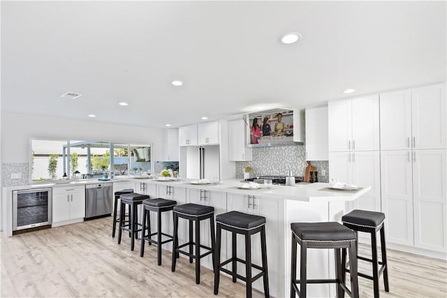 kitchen with white cabinets, stainless steel dishwasher, beverage cooler, and a kitchen breakfast bar