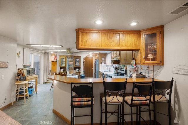 kitchen featuring tasteful backsplash, electric stove, a kitchen breakfast bar, kitchen peninsula, and ceiling fan