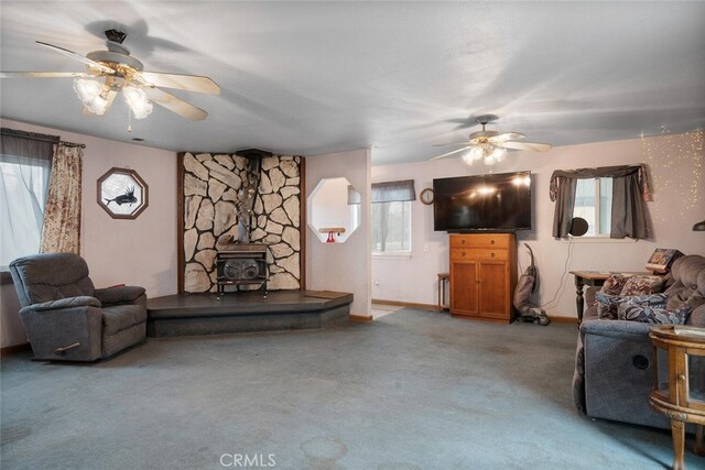 carpeted living room featuring ceiling fan, a wealth of natural light, and a wood stove