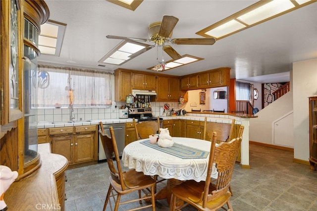 kitchen featuring ceiling fan, kitchen peninsula, sink, appliances with stainless steel finishes, and tile counters