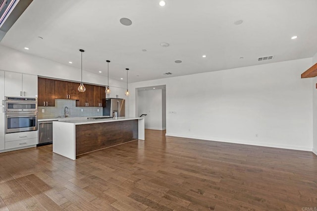 kitchen featuring white cabinetry, an island with sink, stainless steel appliances, decorative backsplash, and decorative light fixtures