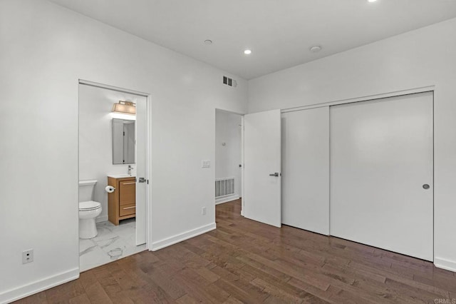 unfurnished bedroom with a closet, connected bathroom, and dark hardwood / wood-style floors