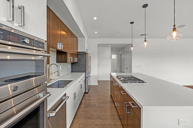 kitchen with appliances with stainless steel finishes, decorative backsplash, a kitchen island, pendant lighting, and sink