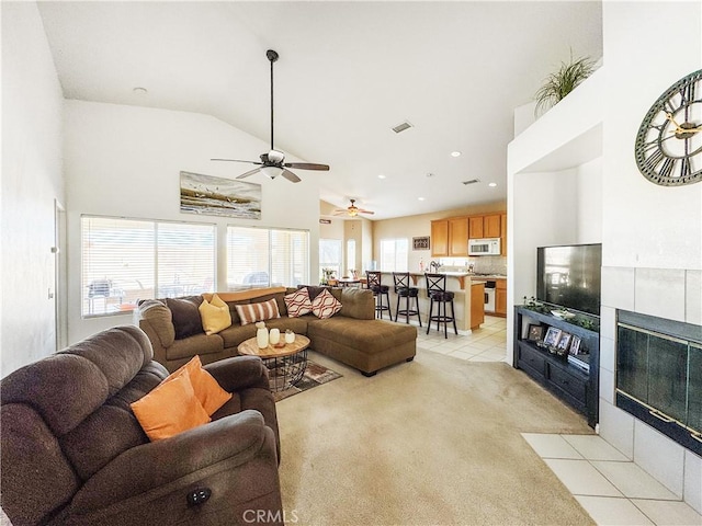 living room with ceiling fan, light colored carpet, a tiled fireplace, and vaulted ceiling