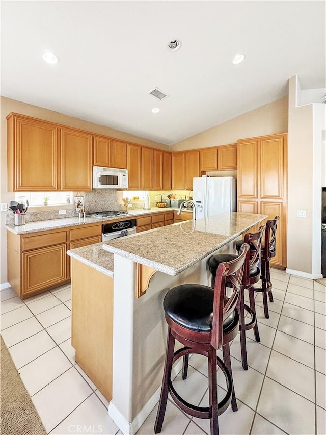 kitchen with appliances with stainless steel finishes, a kitchen island with sink, vaulted ceiling, light tile patterned floors, and a breakfast bar area