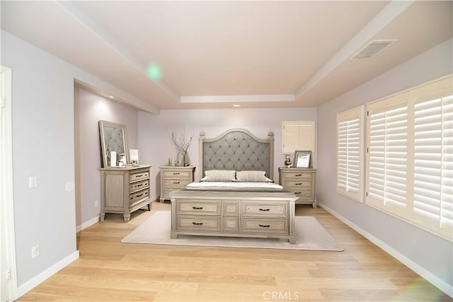 bedroom featuring a raised ceiling and light wood-type flooring