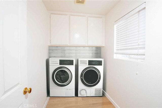 laundry room featuring washer and clothes dryer, light hardwood / wood-style floors, and cabinets