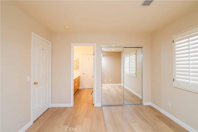 unfurnished bedroom featuring ensuite bathroom, light hardwood / wood-style flooring, and a closet