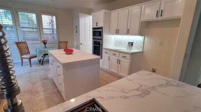 kitchen with light stone counters, stainless steel appliances, a center island, and white cabinets