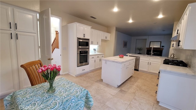 kitchen with appliances with stainless steel finishes, kitchen peninsula, a kitchen island, decorative backsplash, and white cabinets