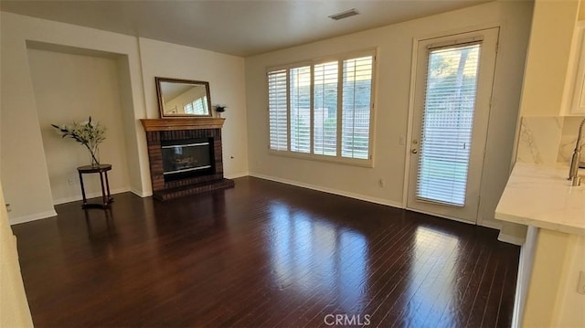 unfurnished living room with a brick fireplace and dark wood-type flooring