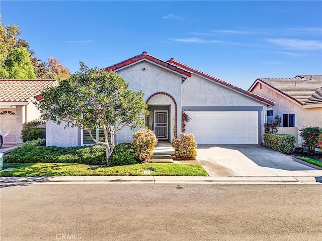 mediterranean / spanish-style house featuring driveway, a tiled roof, a garage, and stucco siding