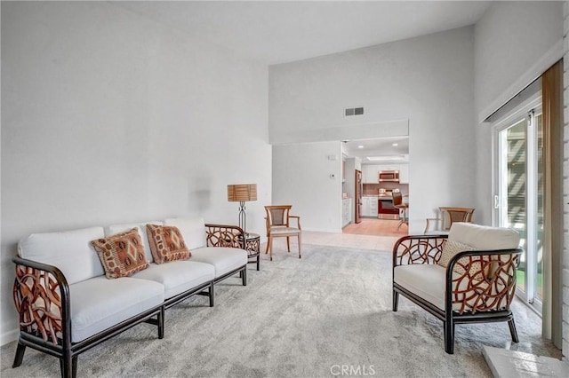 living area with a towering ceiling, visible vents, and light colored carpet